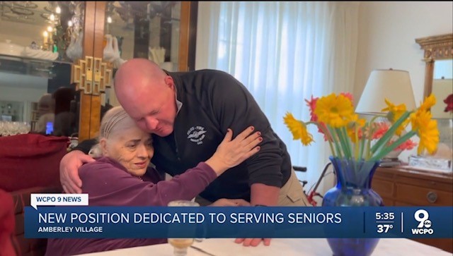 Officer hugging elderly woman who is seated at a table and is hugging him back